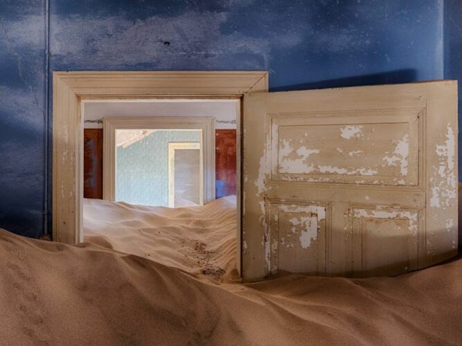 Inside an abandoned building in Kolmanskop, Namibia, where desert sands reclaim the space, creating a surreal tableau of nature's reclamation amidst human history.