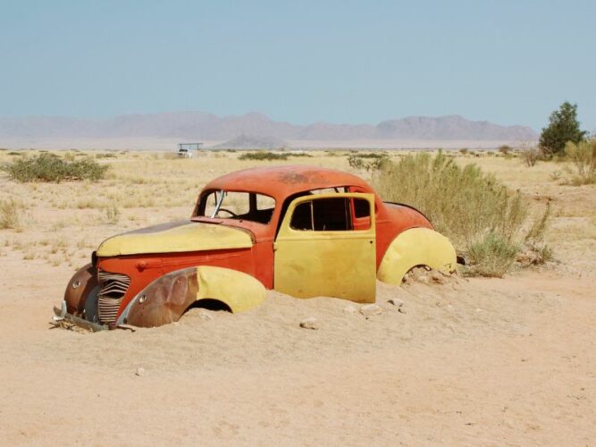 An old, colourful car half-buried in the sand in Solitaire, Namibia, evoking the passage of time in this remote and tranquil desert town.
