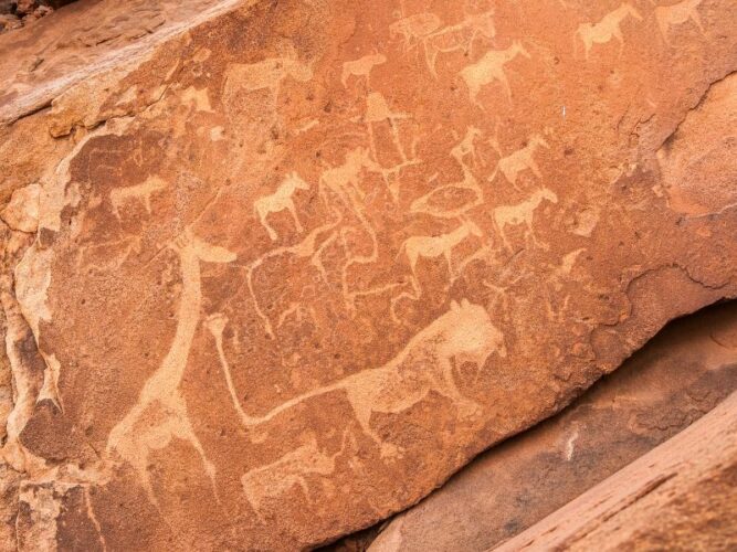Prehistoric rock engravings at Twyfelfontein, Namibia, with depictions of animals and tribal symbols, bearing witness to the area's rich cultural heritage amidst its rugged terrain.