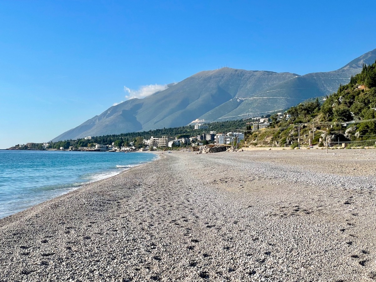 View along Dhermi beach with the green mountains of Llogara National Park rising up into the blue sky