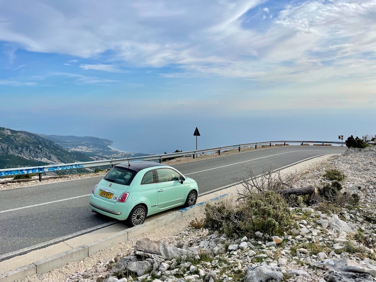 My green Fiat 500 car on the side of the road leading down to the Albanian riviera from the Llogara Pass
