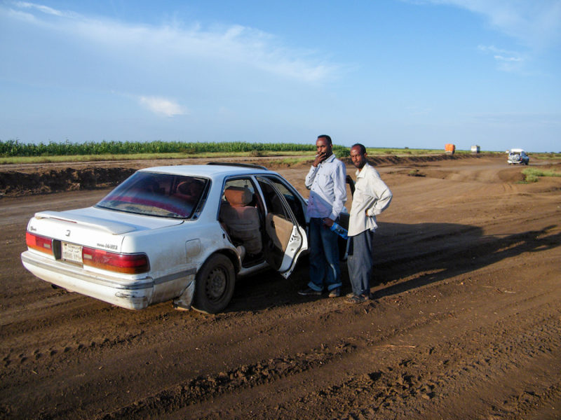 Two men standing outside a white car on a dirt road in Somaliland