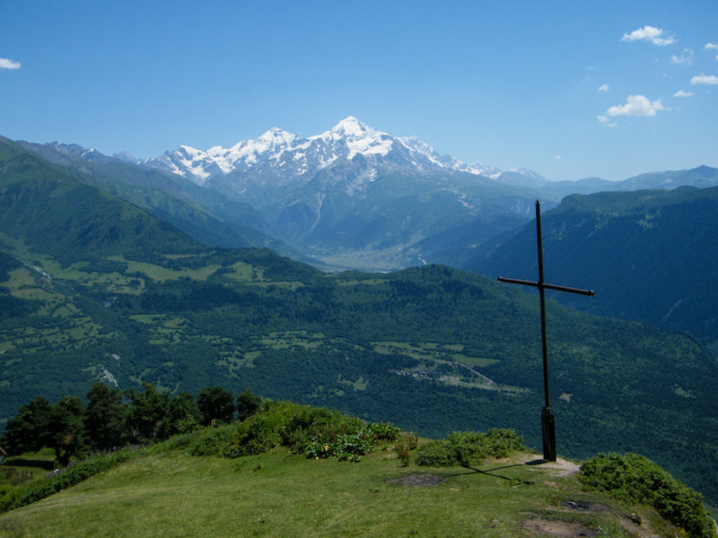 The cross on a hilltop above Mestia with the lush green valley below and snow-covered peaks beyond