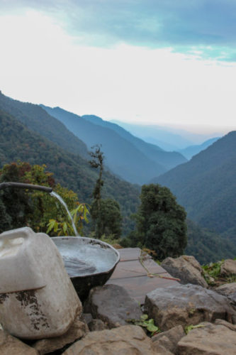 Spring water pouring from a pipe into a metal bowl in the mountains in Sikkim