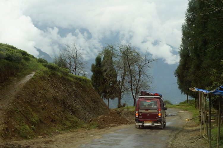 Red shared taxi driving along a road in rural Sikkim under a cloudy sky