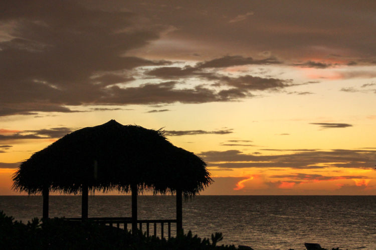 Sunset colours over the sea in Cuba with the silhouette of a thatched beach shelter in the foreground