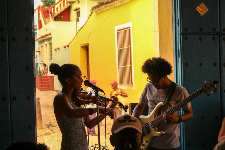 Man playing guitar and woman playing violin in a restaurant bar in Trinidad with an open door behind showing an old yellow building