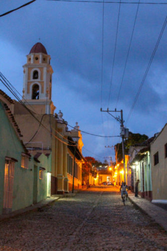 Historic streets of Trinidad at dusk with streetlights casting an atmospheric glow and a yellow and white bell tower rising into the sky