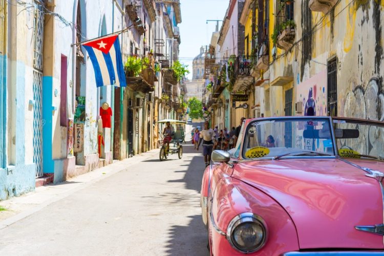 Pink convertible vintage car in old town havana with a cuban flag hanging from the wall of a building