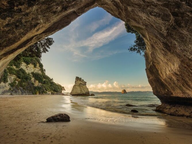 Inside a large sea cave at Cathedral Cove, Hahei with blue sky reflected in the wet sand