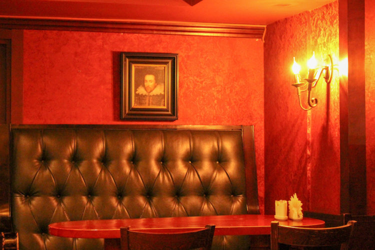 Interior of the Shakespeare pub in Almaty with comfy leather seats, red walls, and a painting of someone who looks like William Shakespeare on the wall