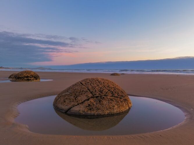 Spherical Moeraki Boulders at Koekohe Beach, New Zealand, with pools of water forming little moats around the rocks