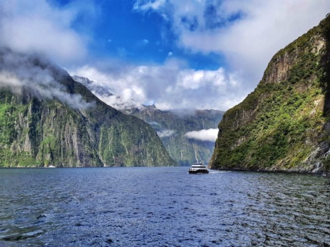 Catamaran tour boat in Milford Sound with clouds hanging part way down the vertical cliffs