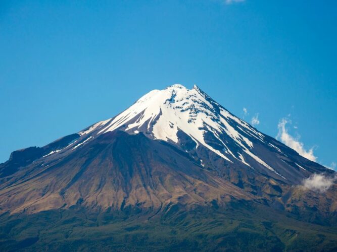 View of Mount Taranaki volcano with snow covered peak and blue sky