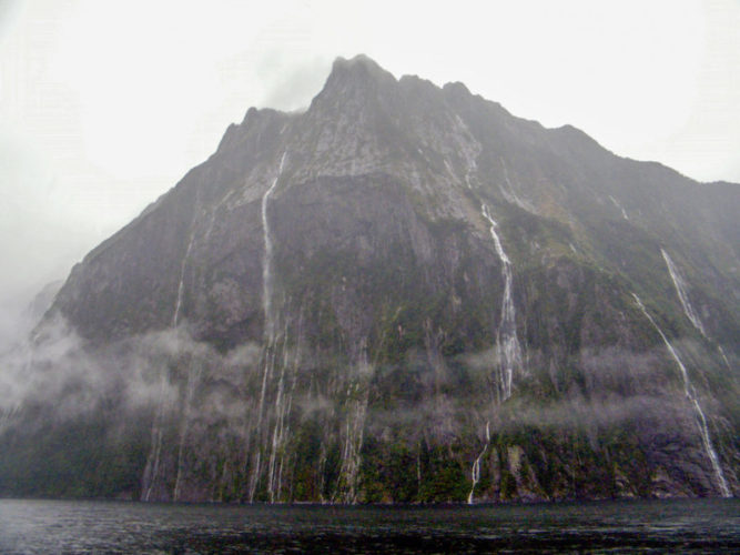 Towering vertical cliffs in Milford Sound with waterfalls tumbling into the sea