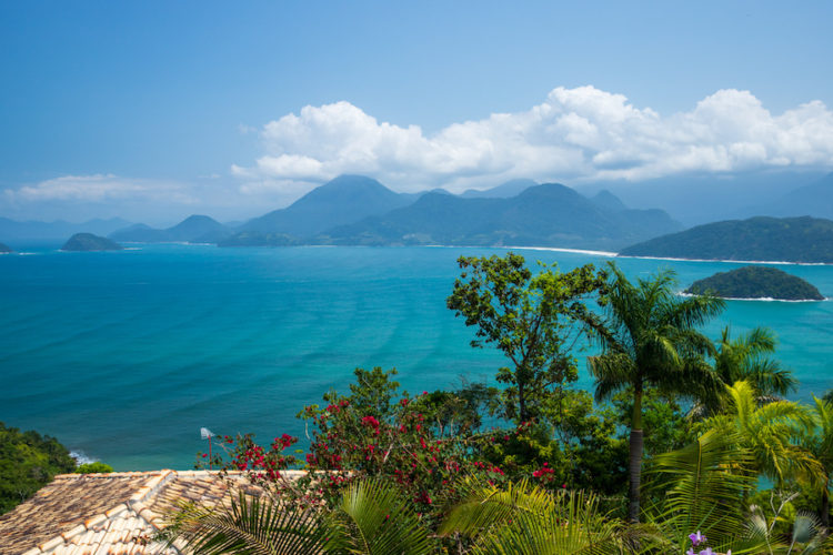 View over the bay from above Praia da Almada with tropical greenery in the foreground, waves rippling in the turquoise sea and pristine beaches and mountains beyond