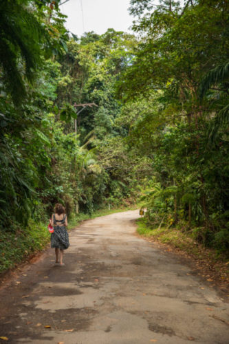 Woman-walking-down-the-road-leading-to-Praia-da-Almada-surrounded-by-lush-tropical-greenery