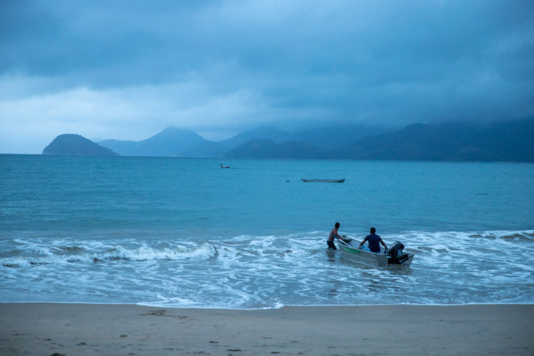 Two men on a beach pushing a boat into the sea at sunset on a moody cloudy day