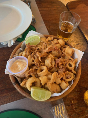 Fried squid in a bowl with slices of lime and spicy mayo and a half-full glass of beer