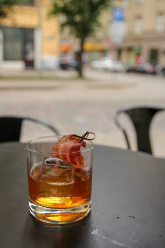 Old fashioned cocktail with bacon garnish on a table outside a bar in Riga