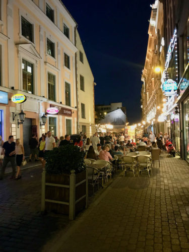 The Old Town of Riga at night with people sitting at tables outside various restaurants and bars