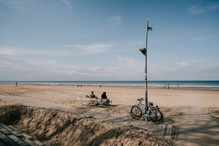 Two bicycles leaning against a lamp post and two people sitting on a bench looking at the sea at the beach in Jurmala