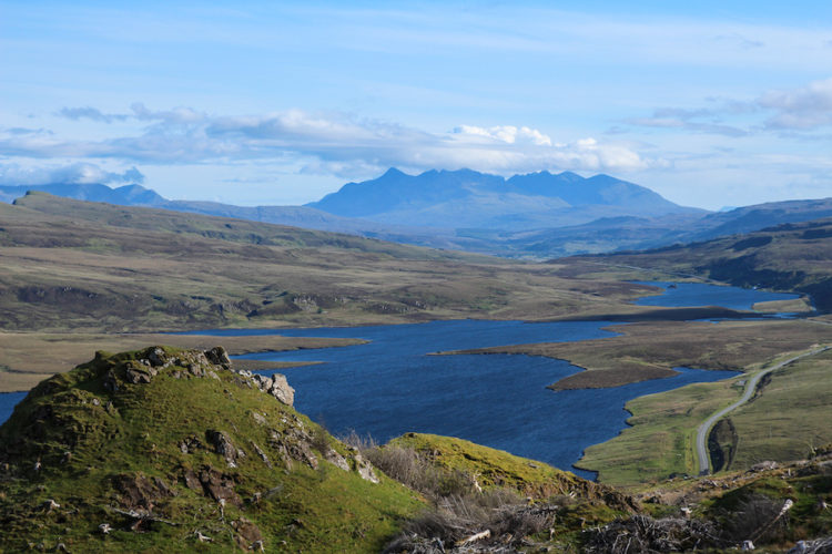View of the torridon hills from the isle of skye with a lake in the middle distance and a grassy hill in the foreground 