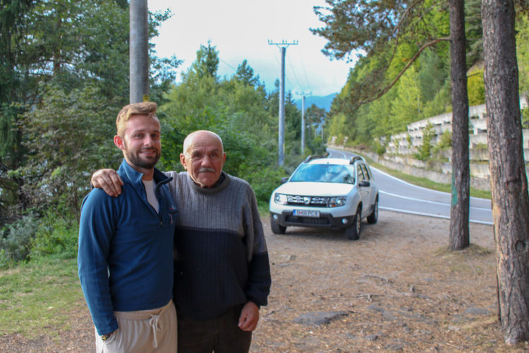 Alex Tiffany making friends with a nice old man and a white car parked by the side of a road while taking a road trip through Romania