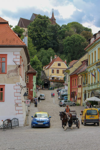 Atmospheric old streets in Sighisoara, Romania with a church at the top of a hill, a horse drawn carriage and cars in the streets below