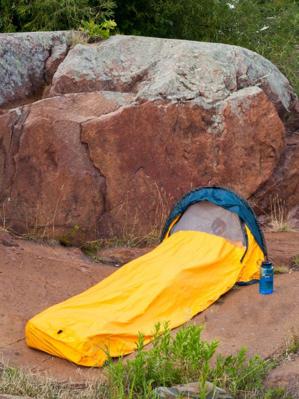 Yellow bivvi tent pitched behind a large orange boulder
