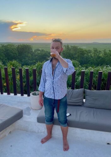 Alex Tiffany drinking a beer on an outdoor terrace at sunset while backpacking in the Yucatan
