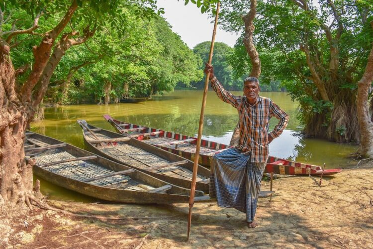 Boatman-standing-next-to-three-wooden-boats-in-the-sundarbans