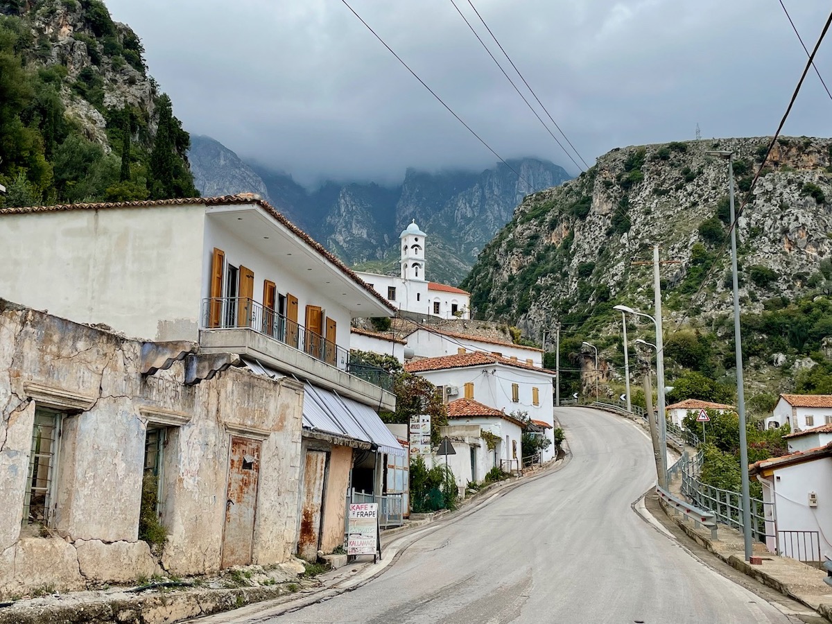 Main road winding through Dhermi village in Albania with attractive old buildings and clouds covering the peaks of the mountains behind