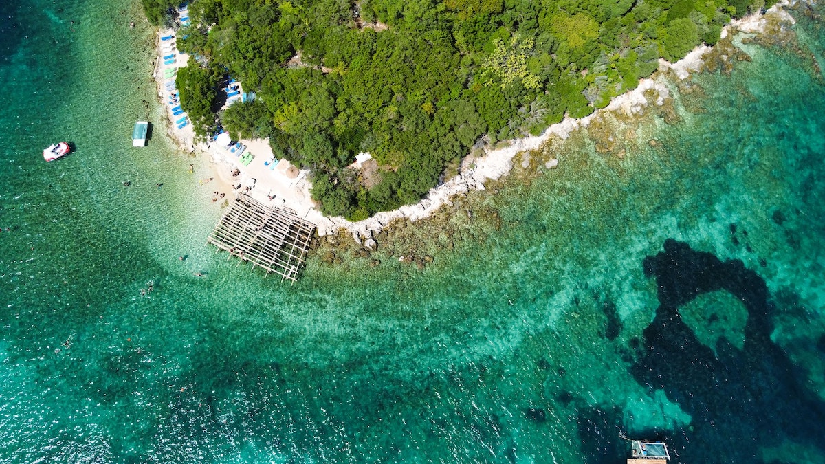 View of one of the Ksamil islands from above with a pristine beach, greenery, and vivid turquoise sea