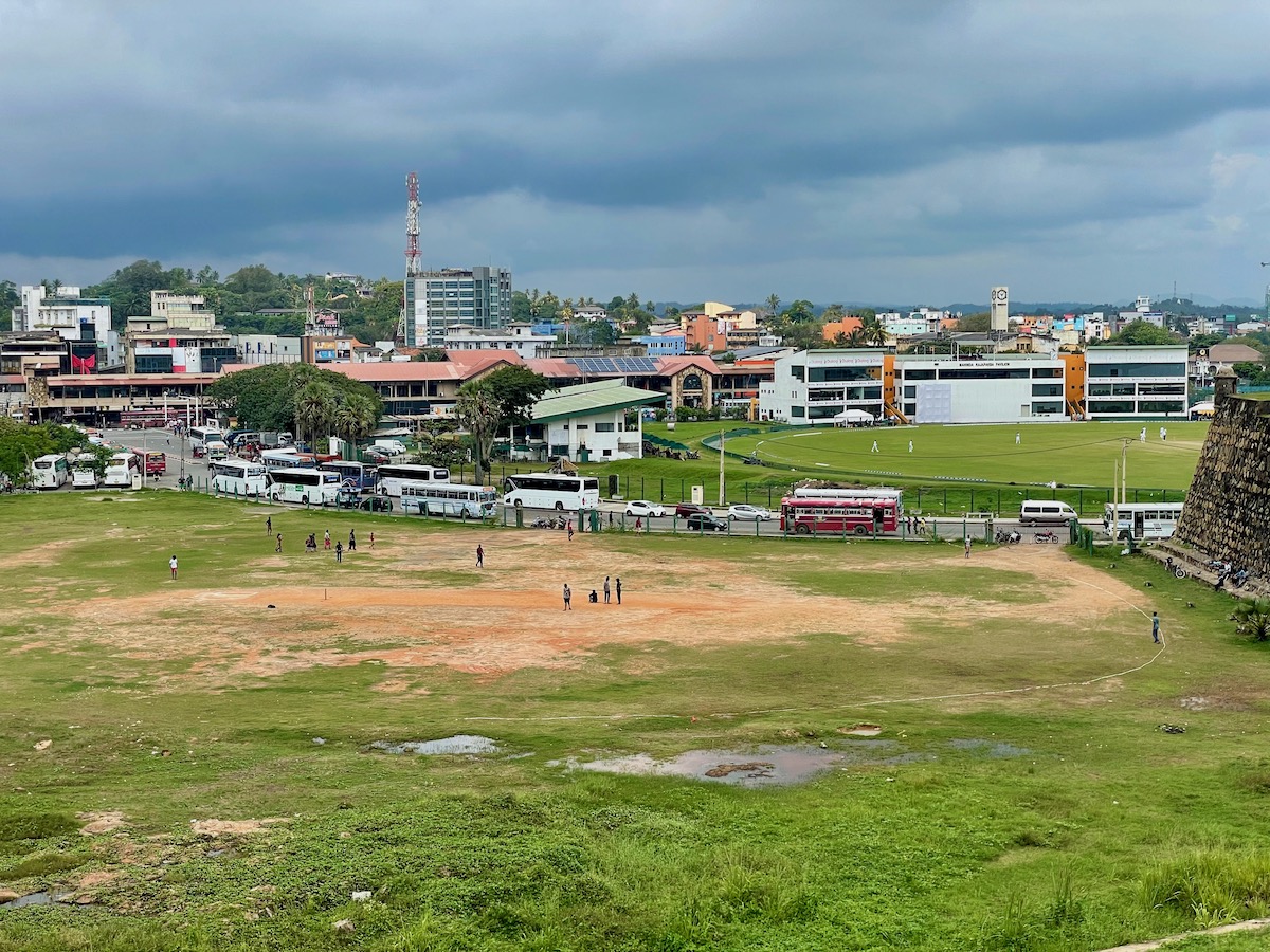 galle international cricket stadium in the background with people playing an informal game of cricket in front