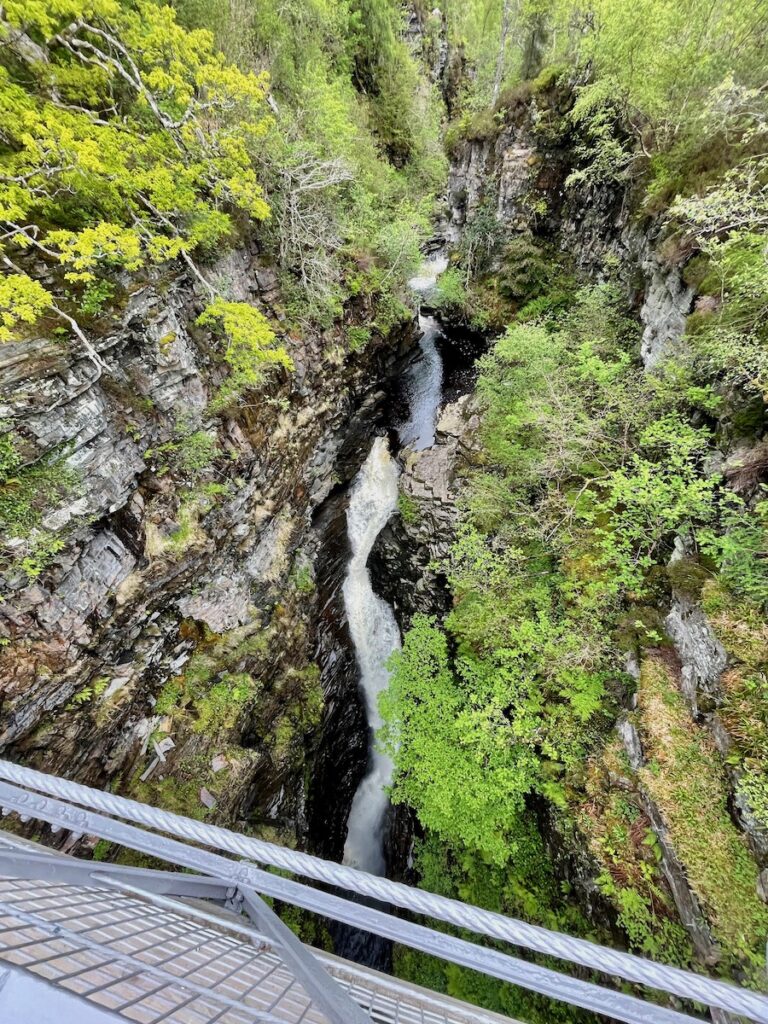 View from the suspension bridge over Corrieshalloch Gorge showing the steep sides lush greenery and powerful waterfall