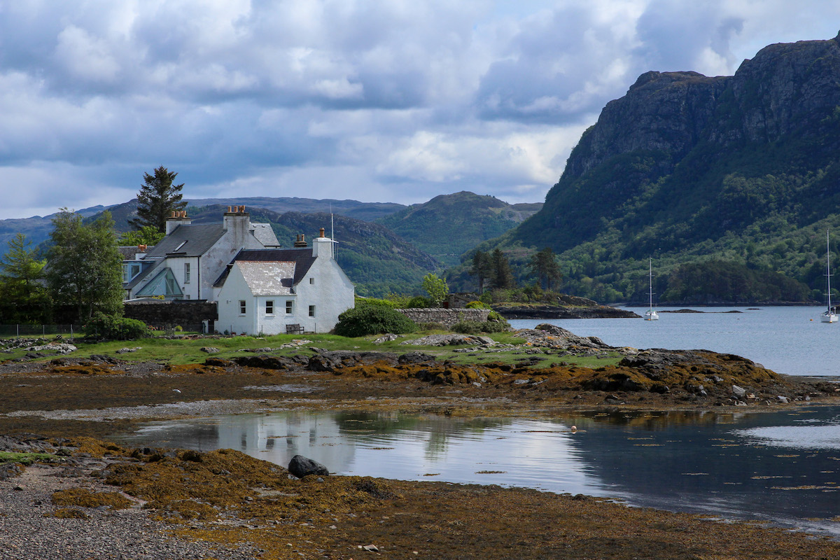 white-cottage-next-to-the-sea-with-mountains-behind-in-scotland
