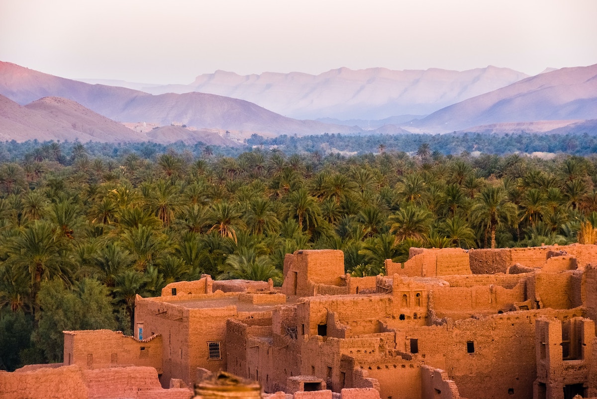 view of Tamnougalt in Morocco with traditional buildings in the foreground and date palms and mountains beyond