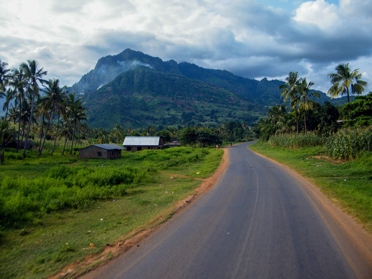 a road passing through rural tanzania with lush green forests and mountains beyond