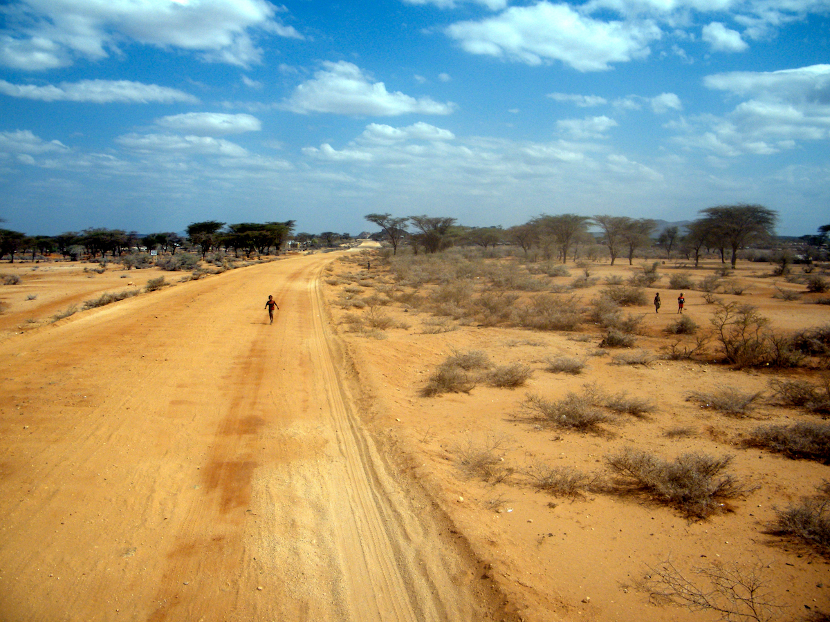 Child running down a sandy dirt road in arid northern Kenya