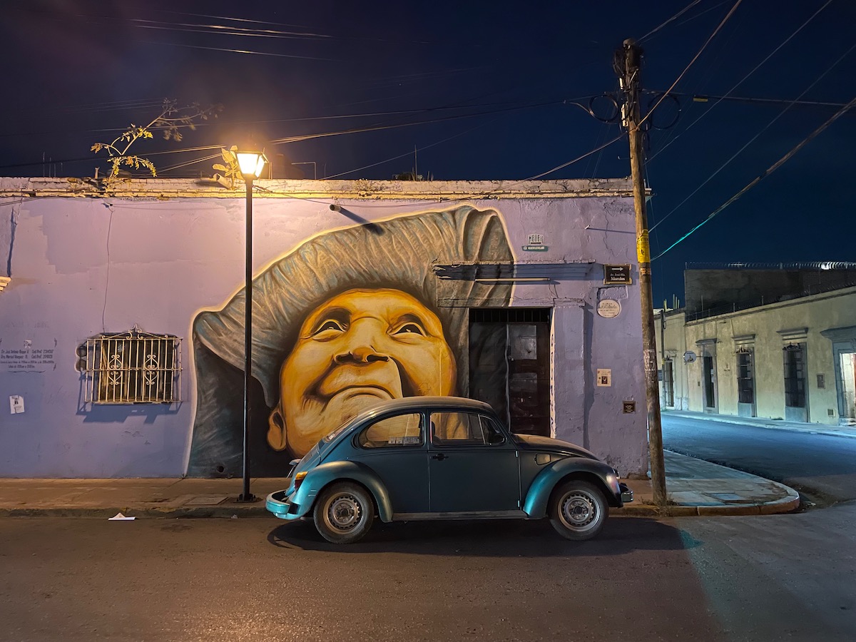 mural of an old woman painted on the wall of a building in oaxaca city with a VW beetle parked infront