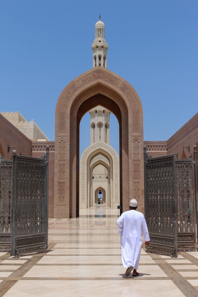 man in white walking through the entrance to the grand mosque in muscat oman