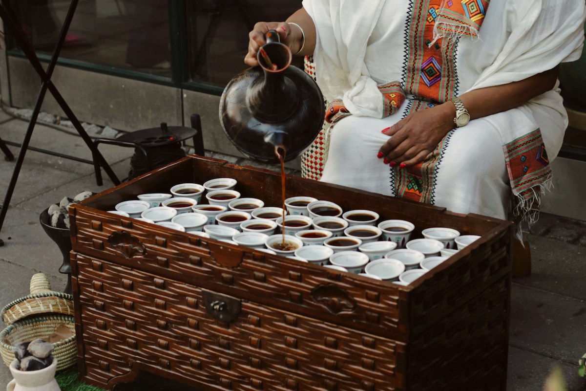 woman pouring coffee from a traditional clay pot into lots of small cups in a traditional ethiopian coffee ceremony