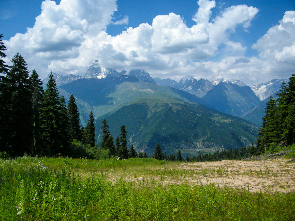 svaneti ski slope near mestia in the summer with alpine grass forests green mountains and blue sky with white clouds