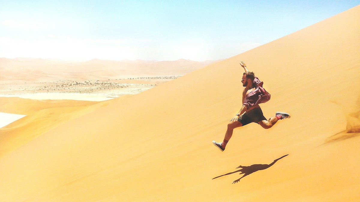 man running down a large yellow sand dune in namibia