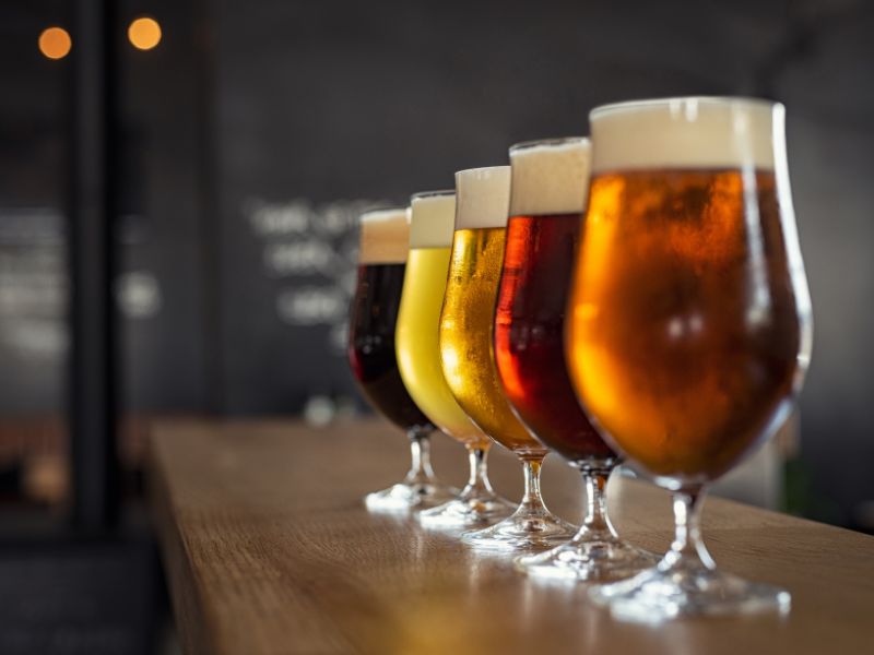 five glasses of different colored craft beer on a wooden bar