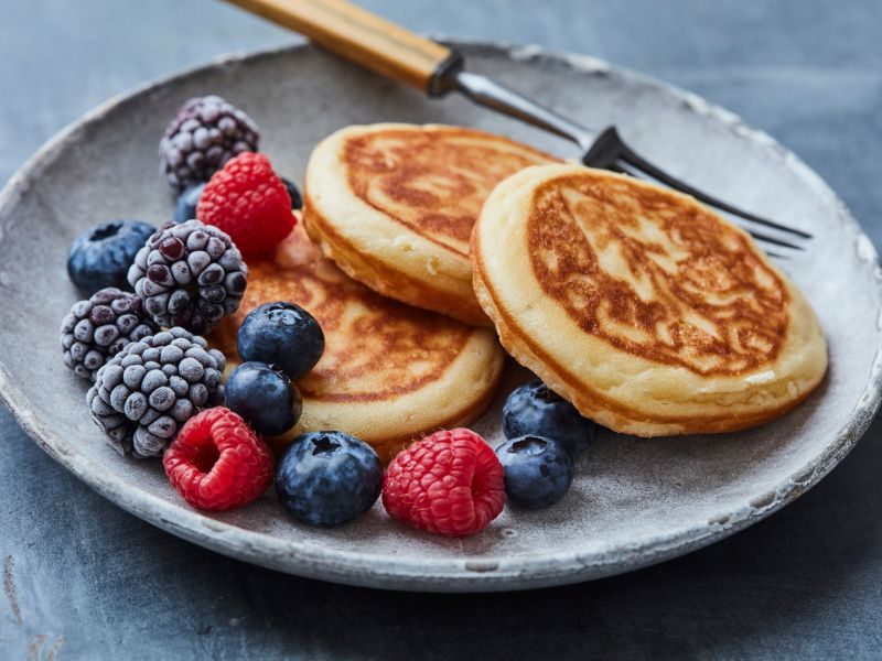 three pancakes and berries arranged on a grey plate