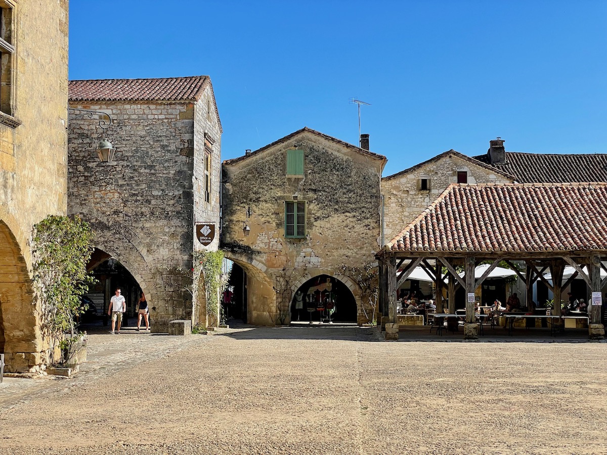 Central town square of Monpazier in Dordogne with medieval buildings and a covered arcade with stone arches running around the edge of the square