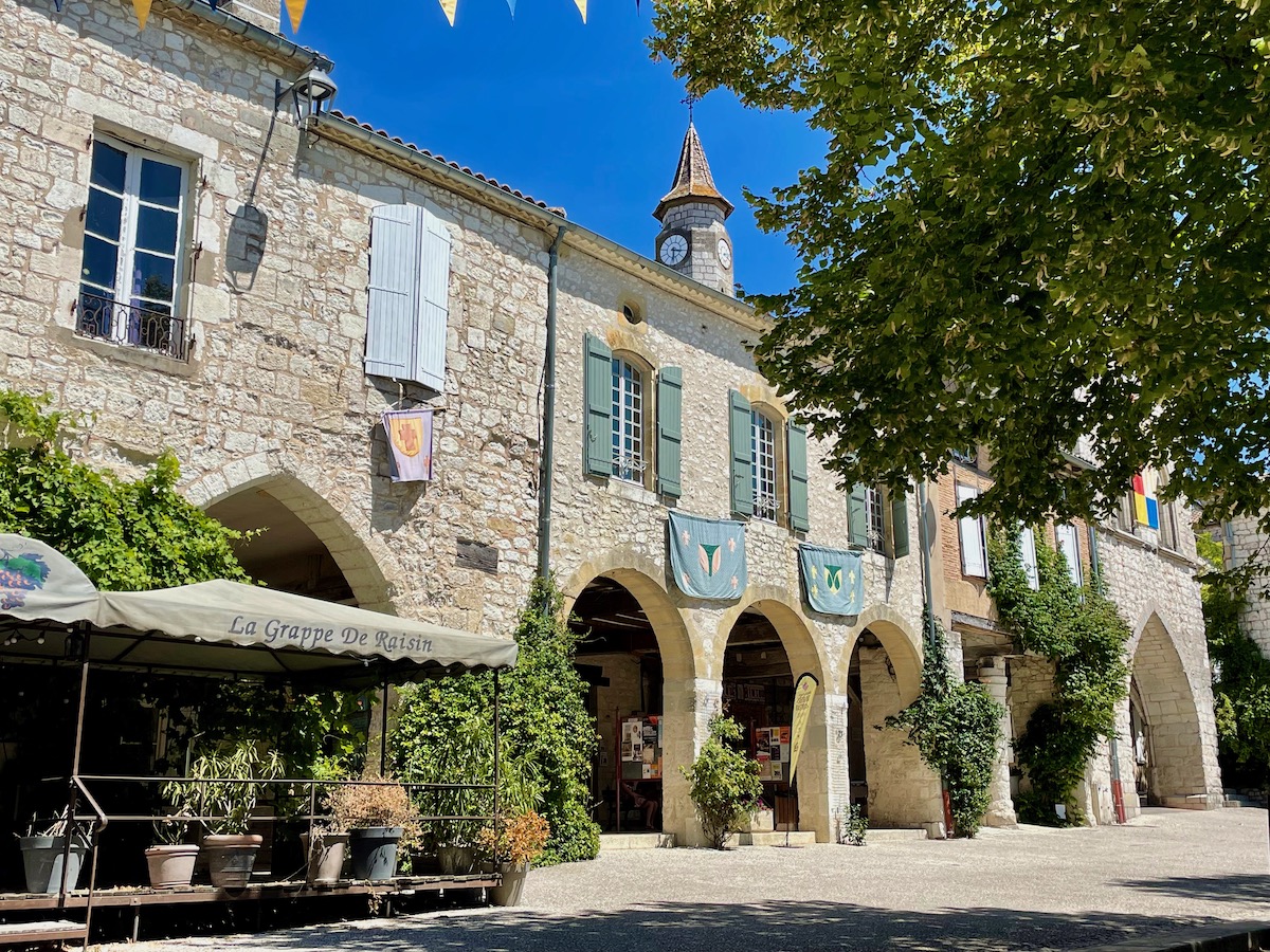 The attractive town square of Monflanquin with lots of greenery and the shaded terrace of a cafe