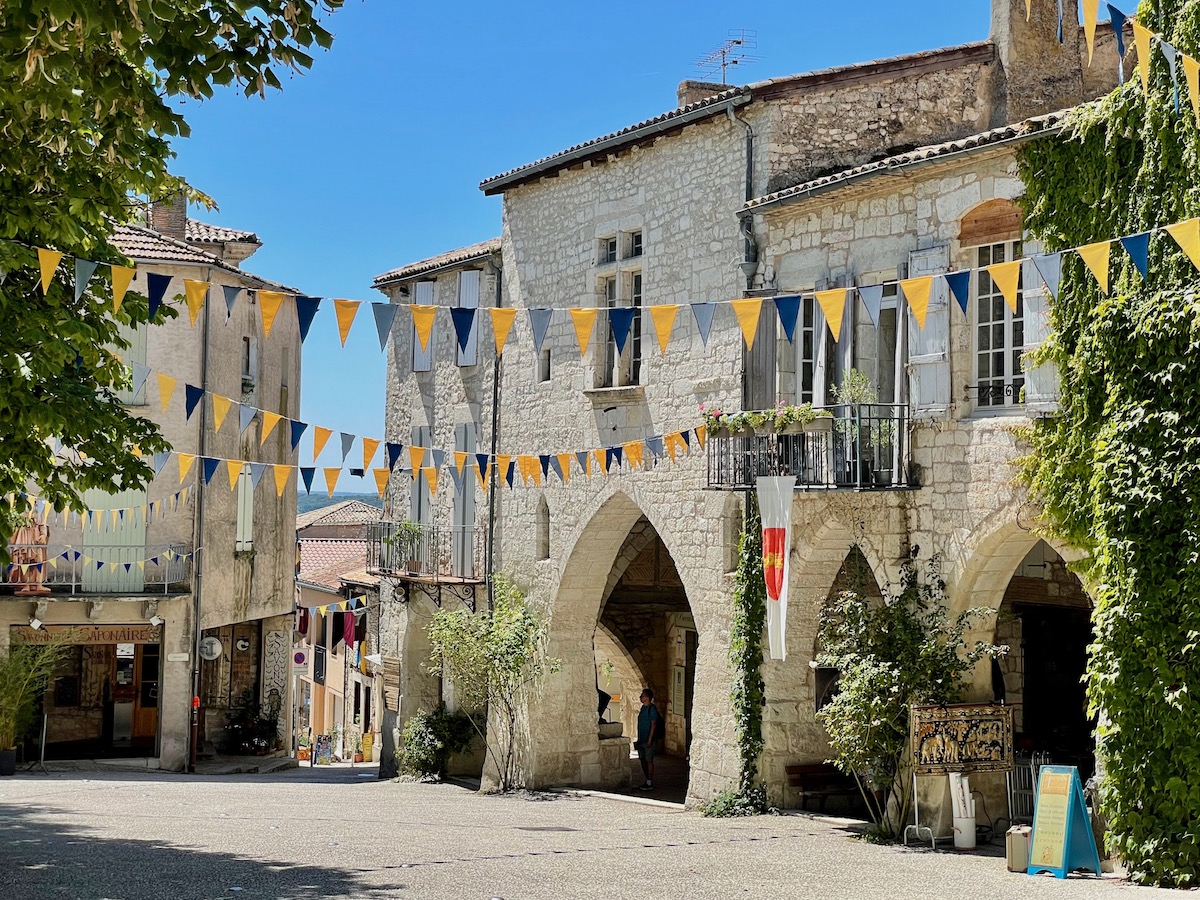 Blue and yellow flags hanging over the street in Monflanquin with old stone buildings and blue skies